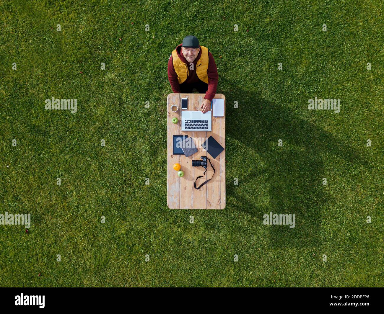 Vista aerea di un uomo seduto al tavolino da caffè prato verde e sorridente alla macchina fotografica Foto Stock