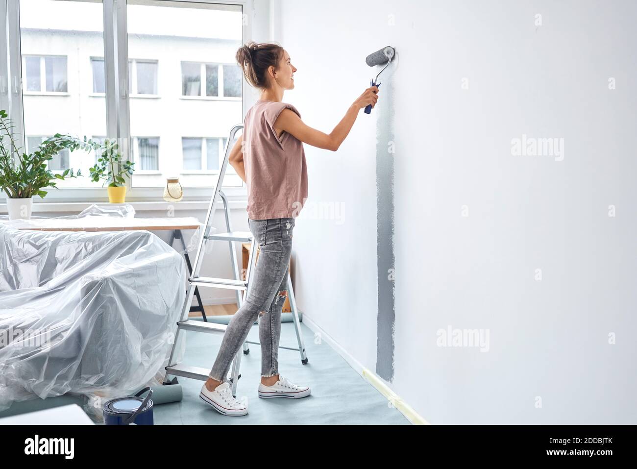 Giovane donna pittura con rullo di vernice sulla parete mentre in piedi a casa Foto Stock