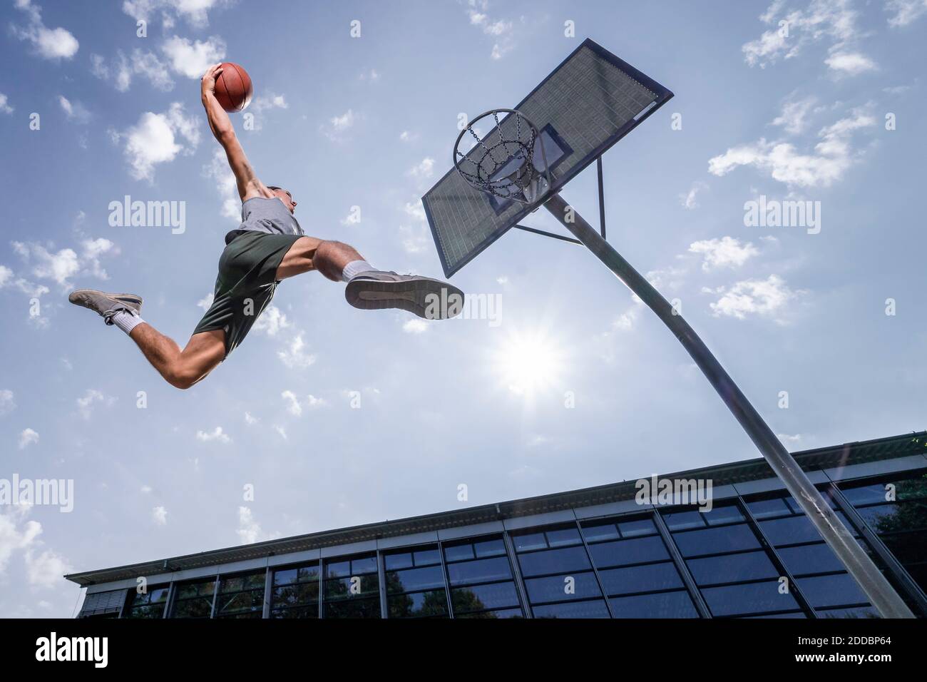 Giovane uomo che dunking palla in cerchio mentre gioca a basket contro cielo in giornata di sole Foto Stock