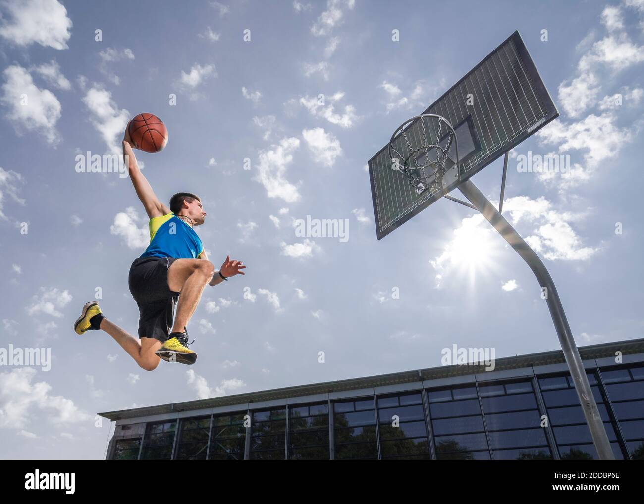 Giovane atleta maschio che dunking palla in cerchio mentre si gioca a basket il giorno di sole Foto Stock