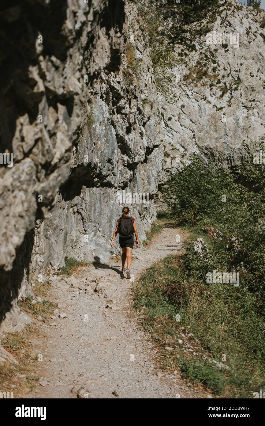 Donna trekking sul sentiero da scogliera rocciosa durante il giorno di sole Foto Stock