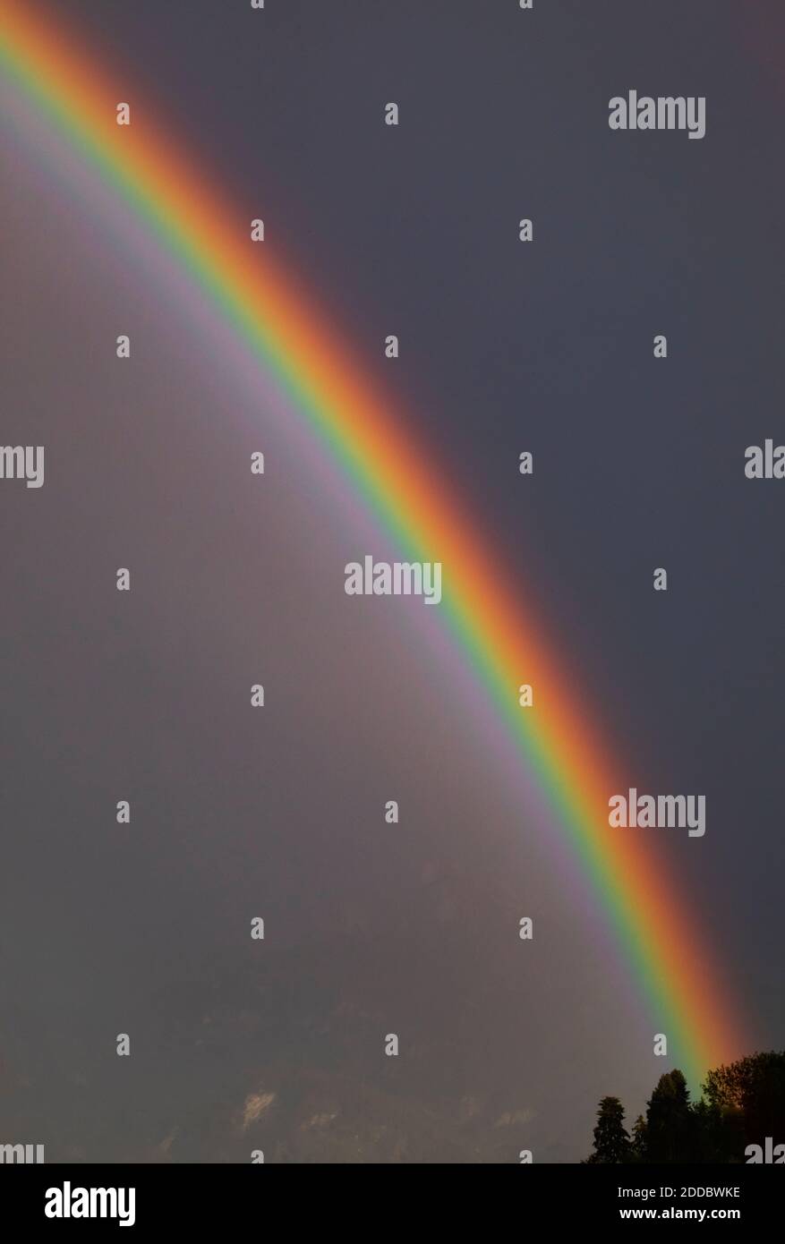 Arcobaleno contro il cielo grigio al crepuscolo Foto Stock