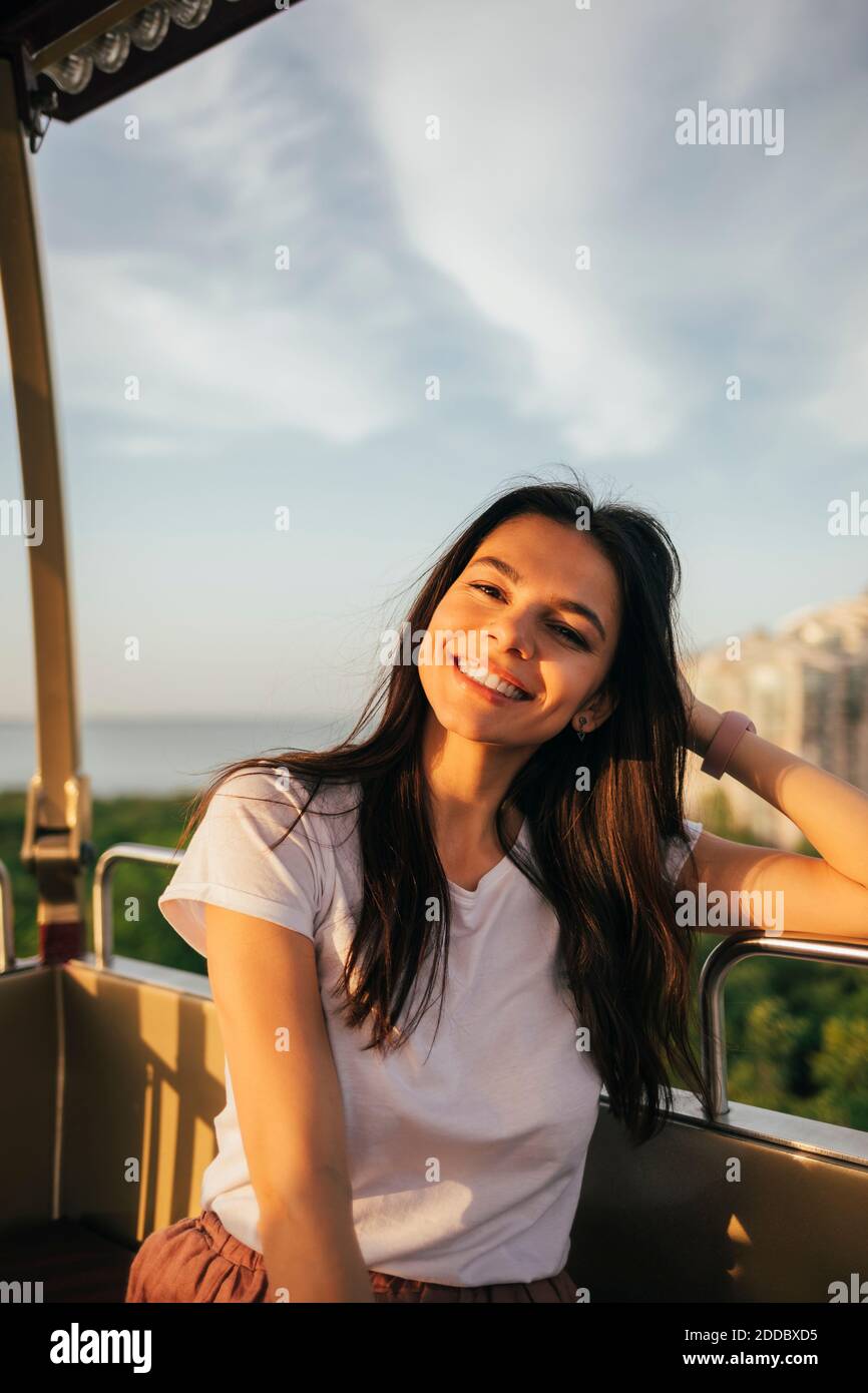 Sorridente bella giovane donna seduta con la mano in capelli godendosi Giro in ruota panoramica Foto Stock
