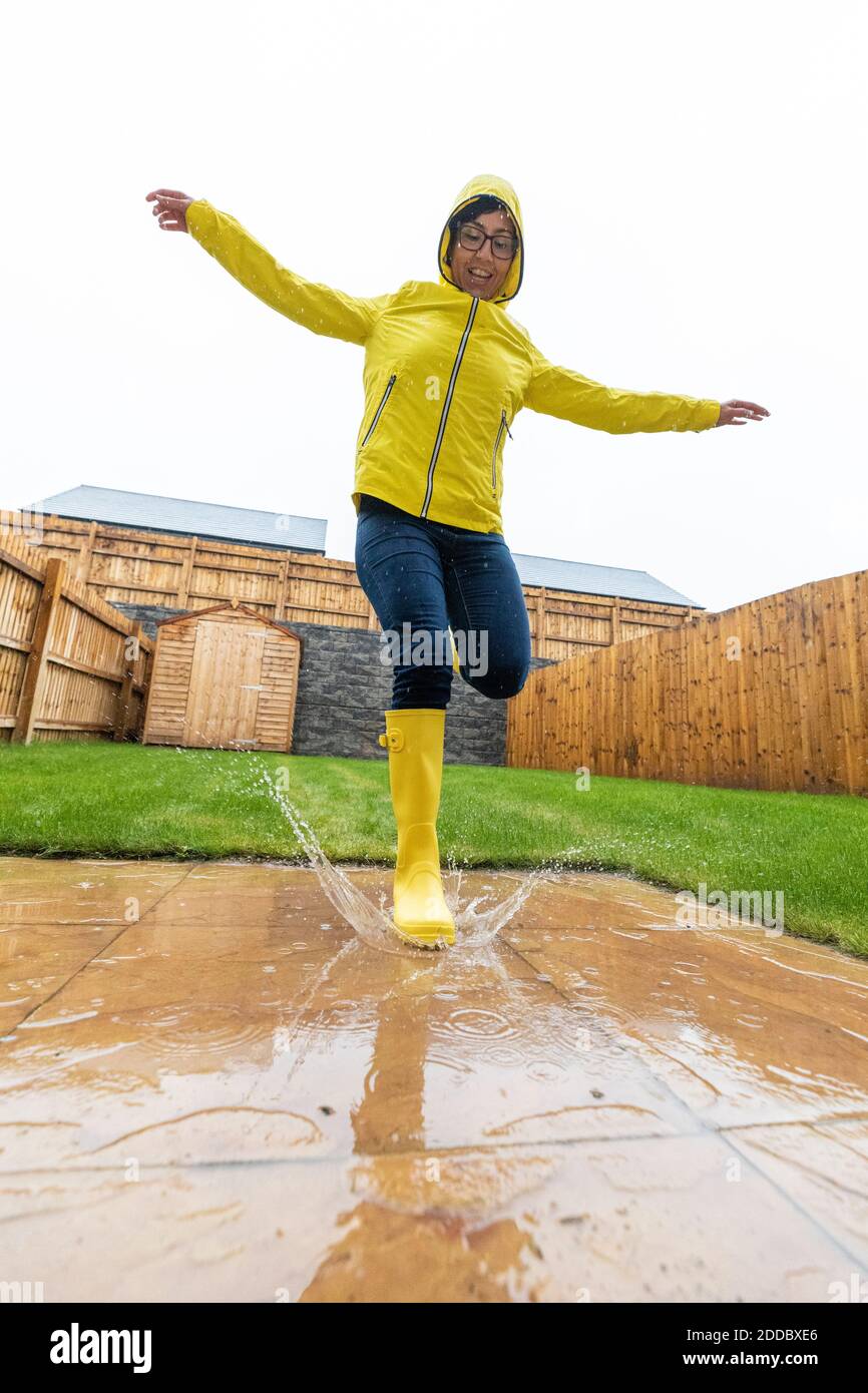Donna che salta in acqua puddle durante la stagione piovosa Foto Stock