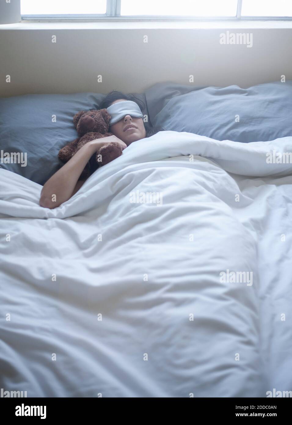 Giovane donna che indossa una maschera per gli occhi che dorme con un giocattolo sul letto a casa Foto Stock Giovane donna che indossa una maschera per gli occhi che dorme con un giocattolo sul letto a casa Foto Stock
