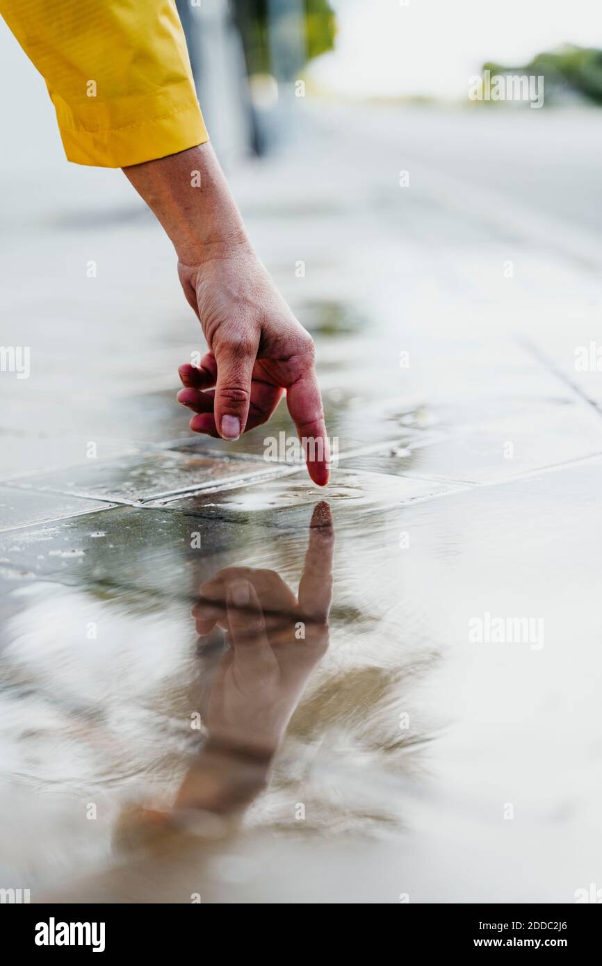 Mano della donna che tocca la pioggia puddle sulla strada Foto Stock