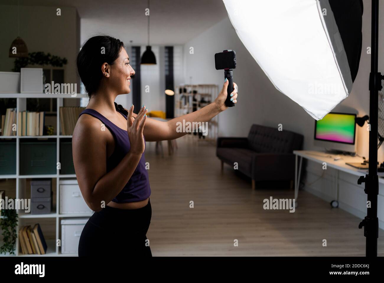 Giovane donna che fa cinque alti mentre la registrazione video davanti di riflettori a casa Foto Stock