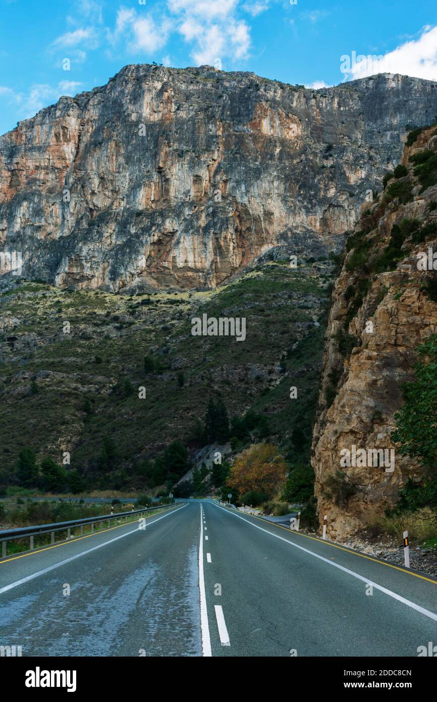 Strada vuota e diritta che corre lungo una grande parete rocciosa. Foto Stock