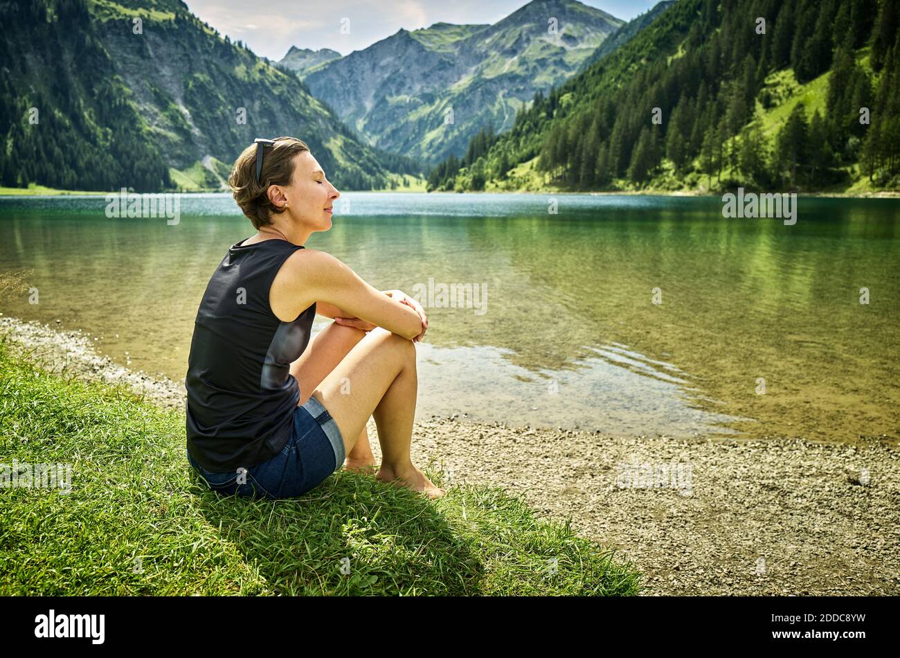 Donna rilassata seduta con gli occhi chiusi sul lago al sole giorno Foto Stock