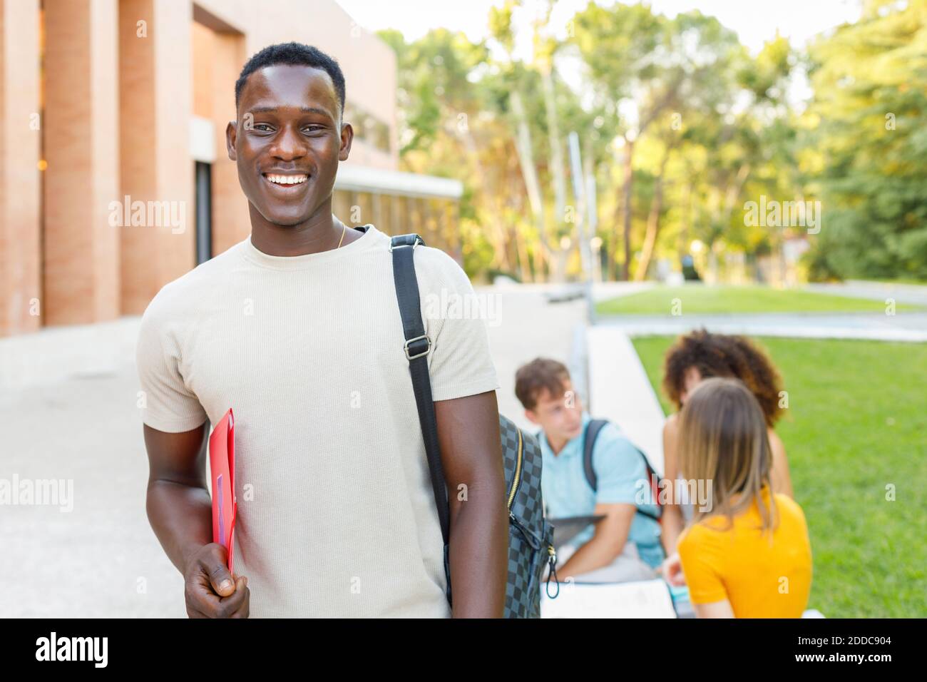 Sorridente studente di sesso maschile sicuro con cartella in piedi nel campus universitario Foto Stock