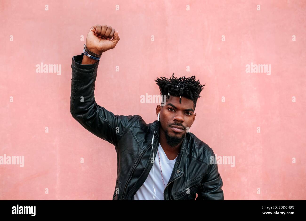 Uomo serio con braccio sollevato ascoltare musica mentre si è in piedi contro parete rosa Foto Stock