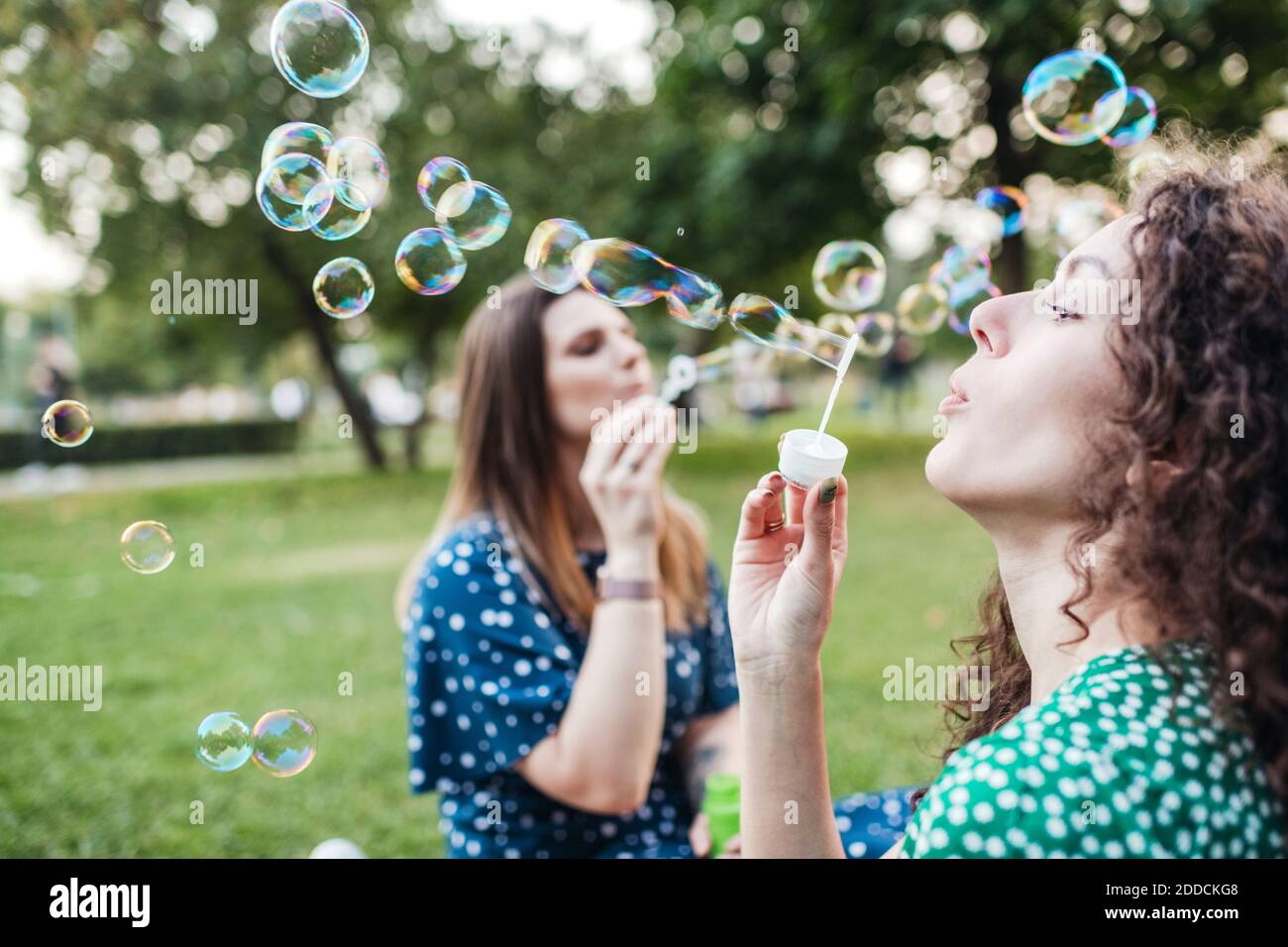 Belle amiche che si godono mentre soffia bolle da wands a. parcheggio Foto Stock