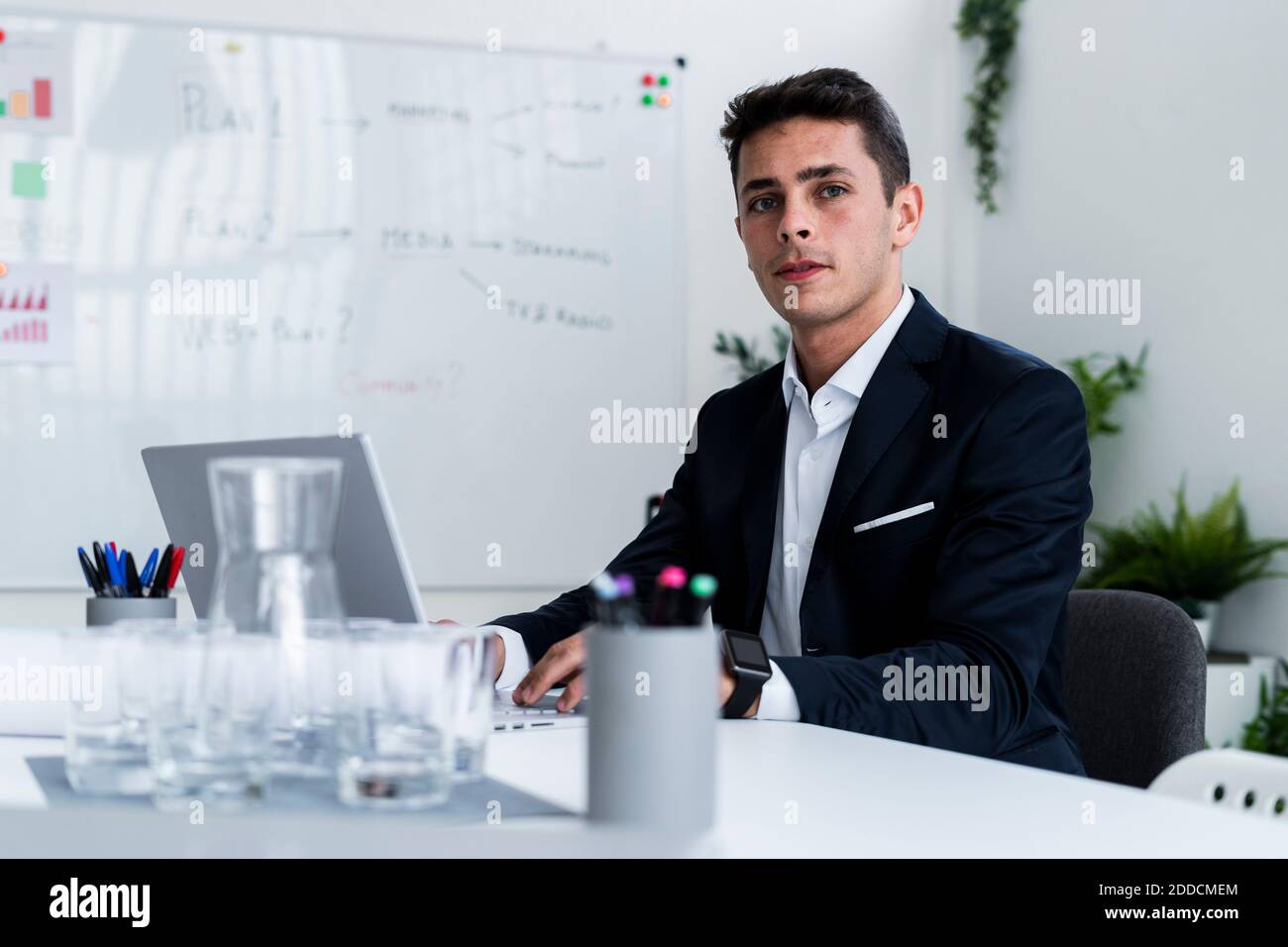 Uomo d'affari sicuro e bello seduto con il computer portatile alla scrivania in creativo luogo di lavoro Foto Stock