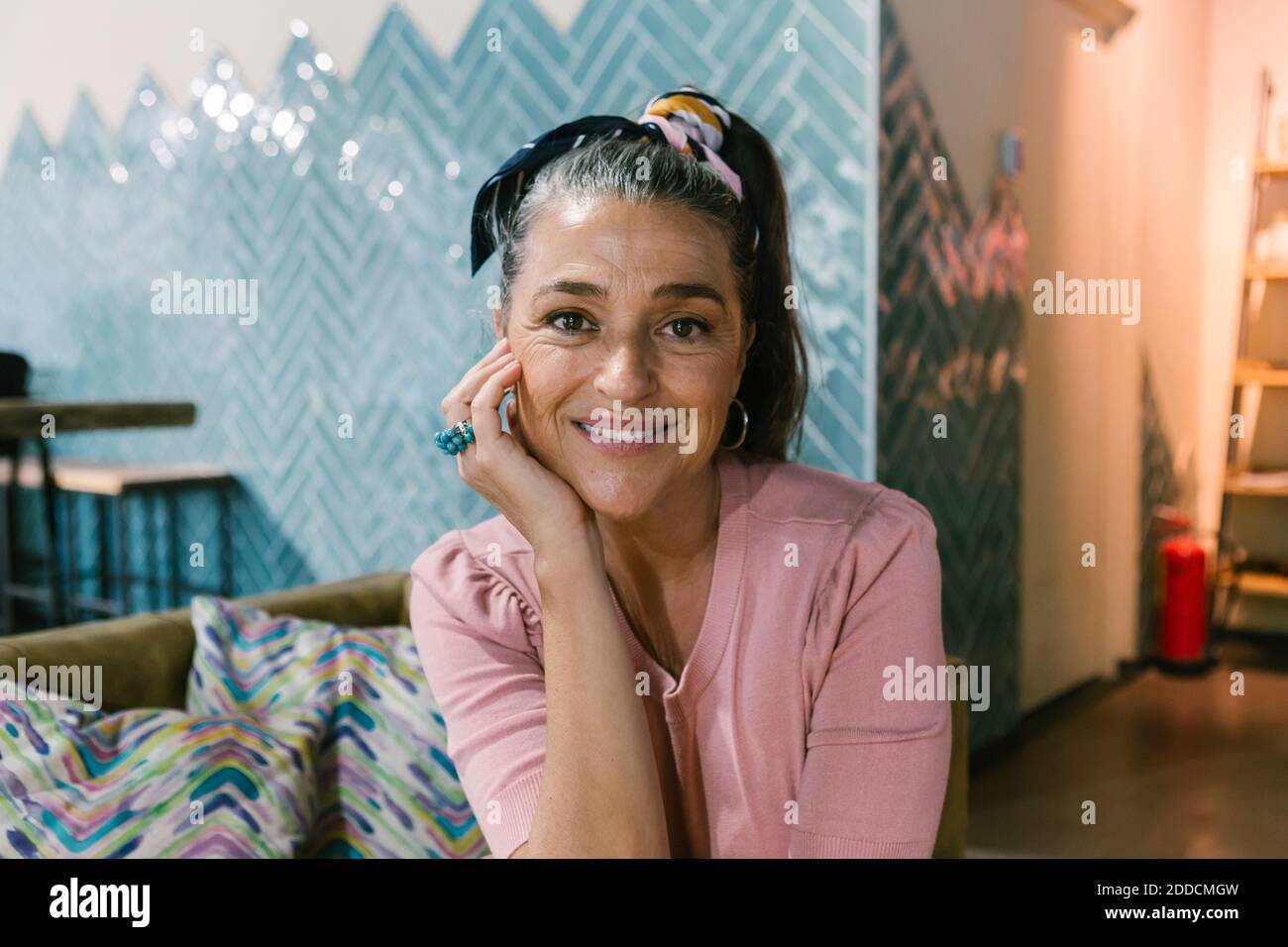 Donna matura sorridente seduta con la mano sul mento al caffè Foto Stock