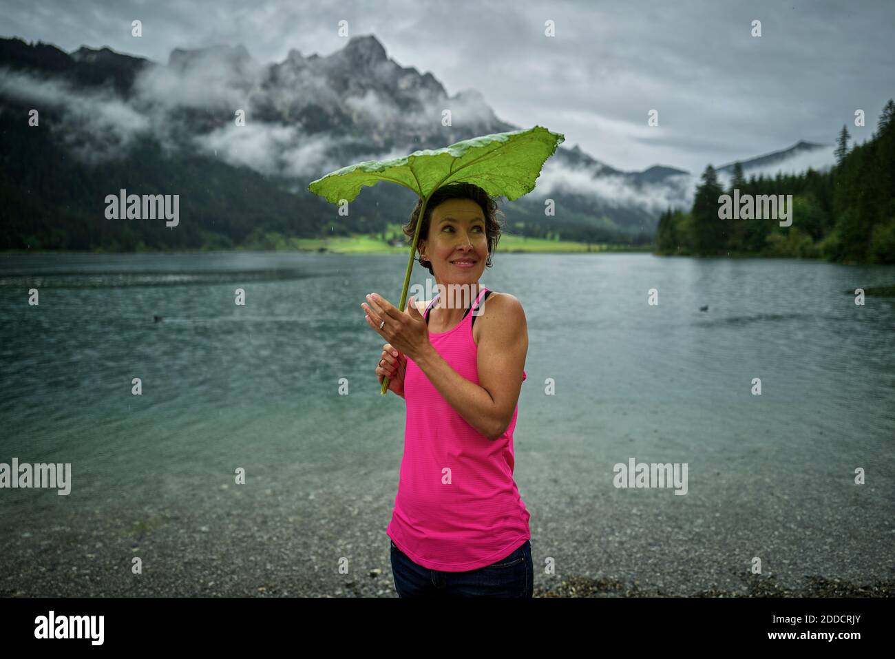 Donna sorridente che tiene la foglia verde mentre si trova a Haldensee Lakeshore durante la stagione delle piogge Foto Stock