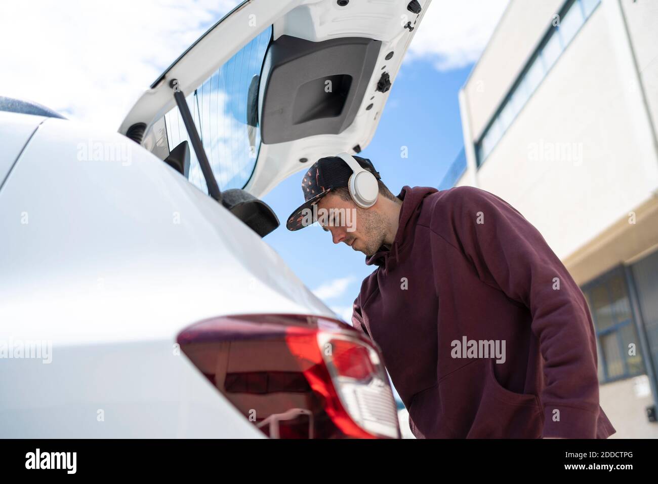 Uomo medio adulto che guarda all'interno del bagagliaio dell'auto mentre si è in piedi giorno di sole Foto Stock