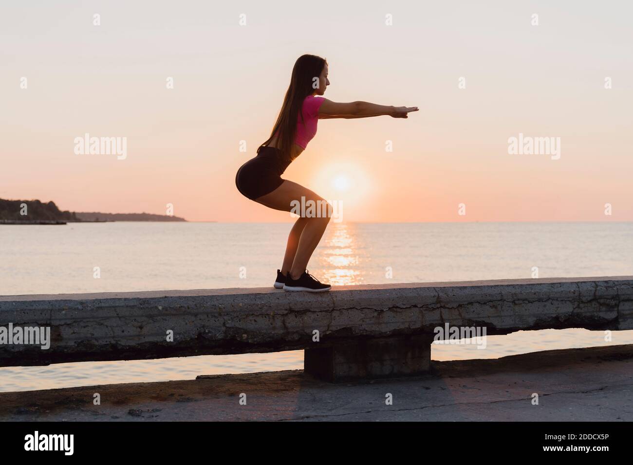 Donna sportiva accovacciata mentre si trova su una parete di cemento contro il mare Foto Stock