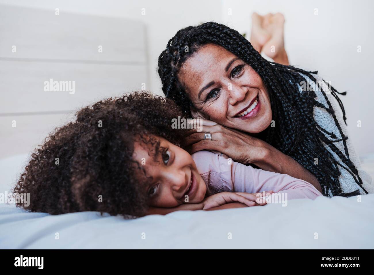 Madre sorridente e figlia che giacciono sul davanti in camera da letto a. casa Foto Stock