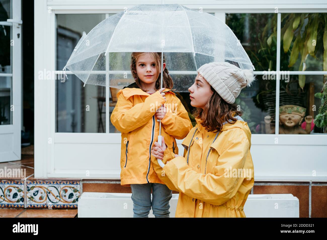 Sorella che guarda la ragazza che tiene l'ombrello mentre si sta in piedi sulla panca Foto Stock