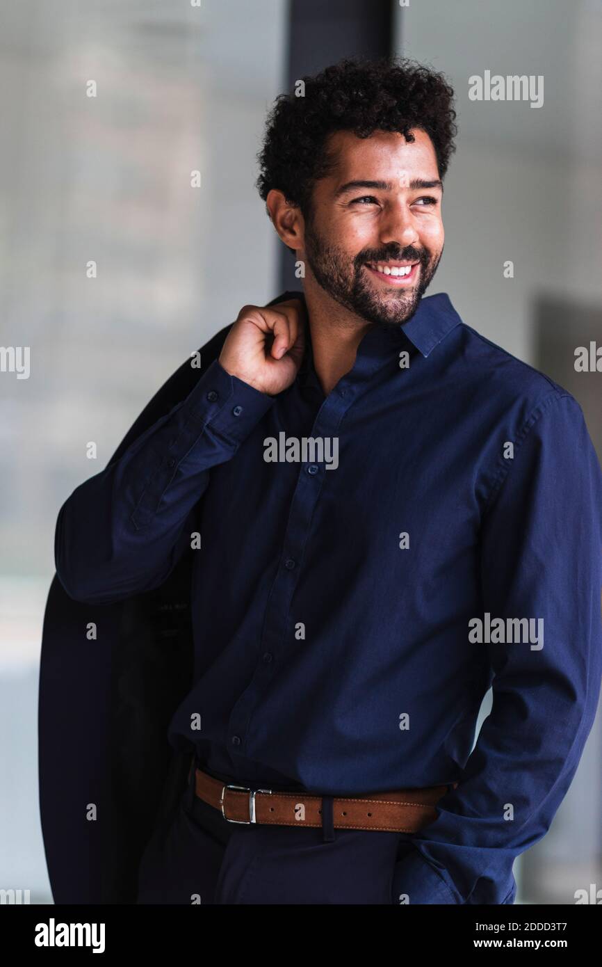 Uomo d'affari sorridente che tiene il blazer mentre si trova in città Foto Stock