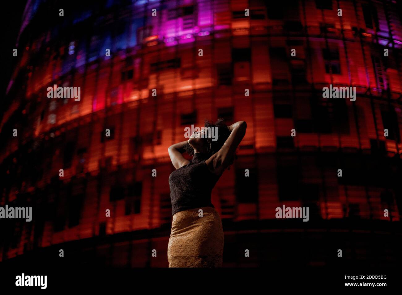 Donna con le braccia sollevate in piedi contro rosso illuminato edificio in città Foto Stock