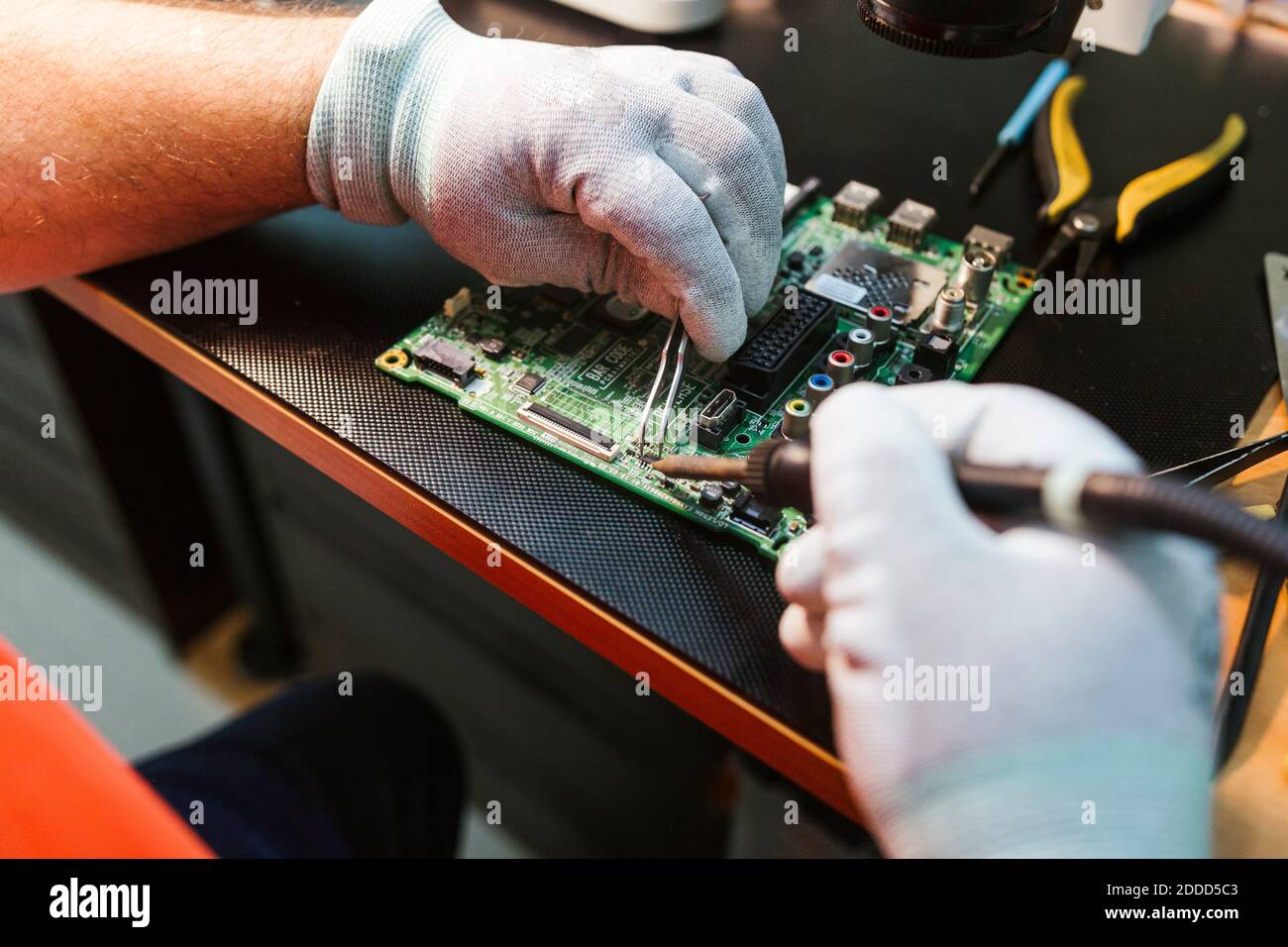 Il tecnico deve saldare il circuito stampato del componente elettrico sul banco di lavoro officina di riparazione elettronica Foto Stock