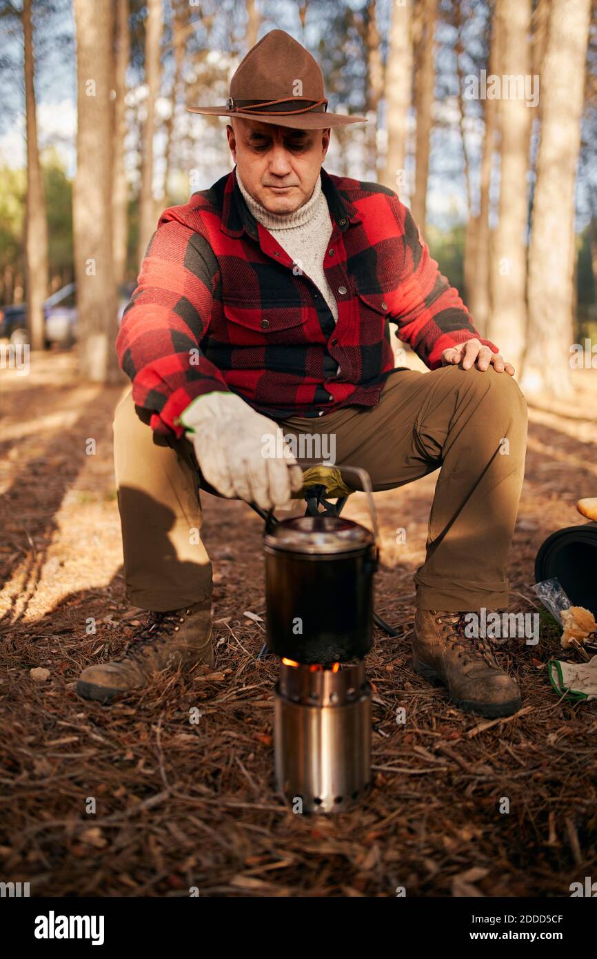 Cucina Bushcrafter su fornello da campeggio mentre si siede in foresta Foto Stock