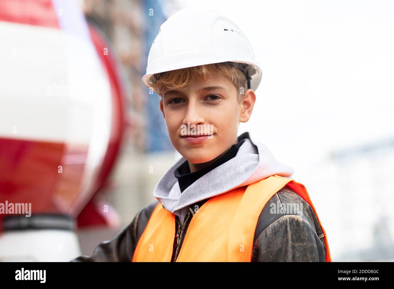 Ragazzo sicuro che indossa un hardhat e vestiti riflettenti a. cantiere Foto Stock