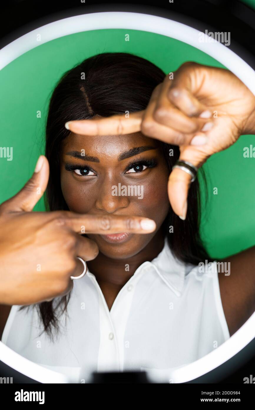 Giovane donna che fa cornice dito contro sfondo verde Foto Stock