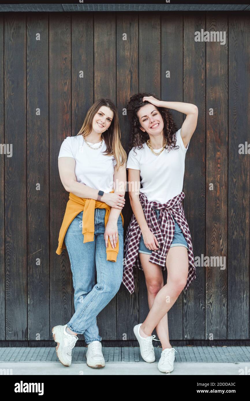 Felici belle donne appoggiate contro il muro di legno marrone Foto Stock