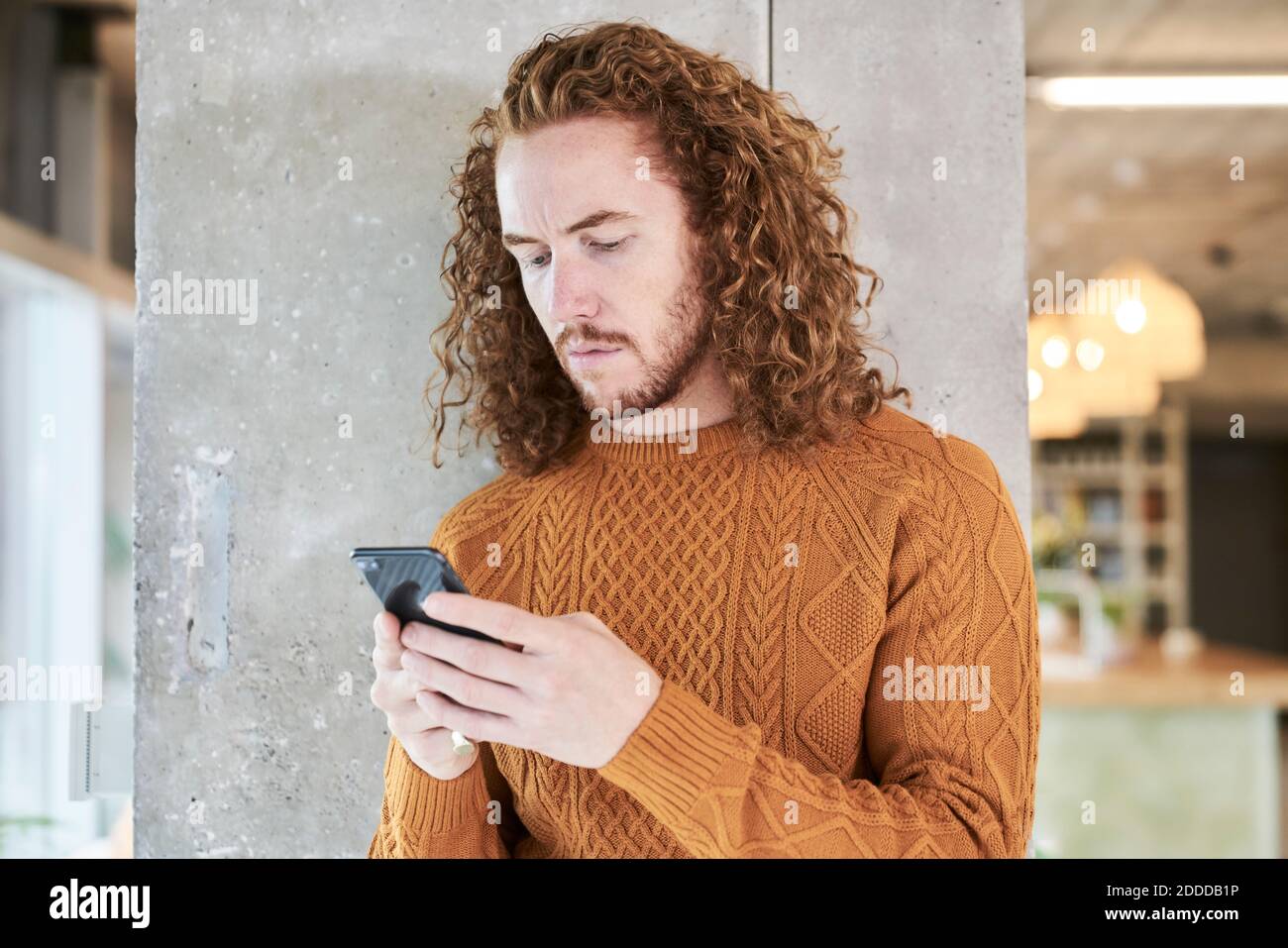 Messaggi di testo Hipster MAN su smartphone in posizione grigia colonna in soggiorno a casa Foto Stock
