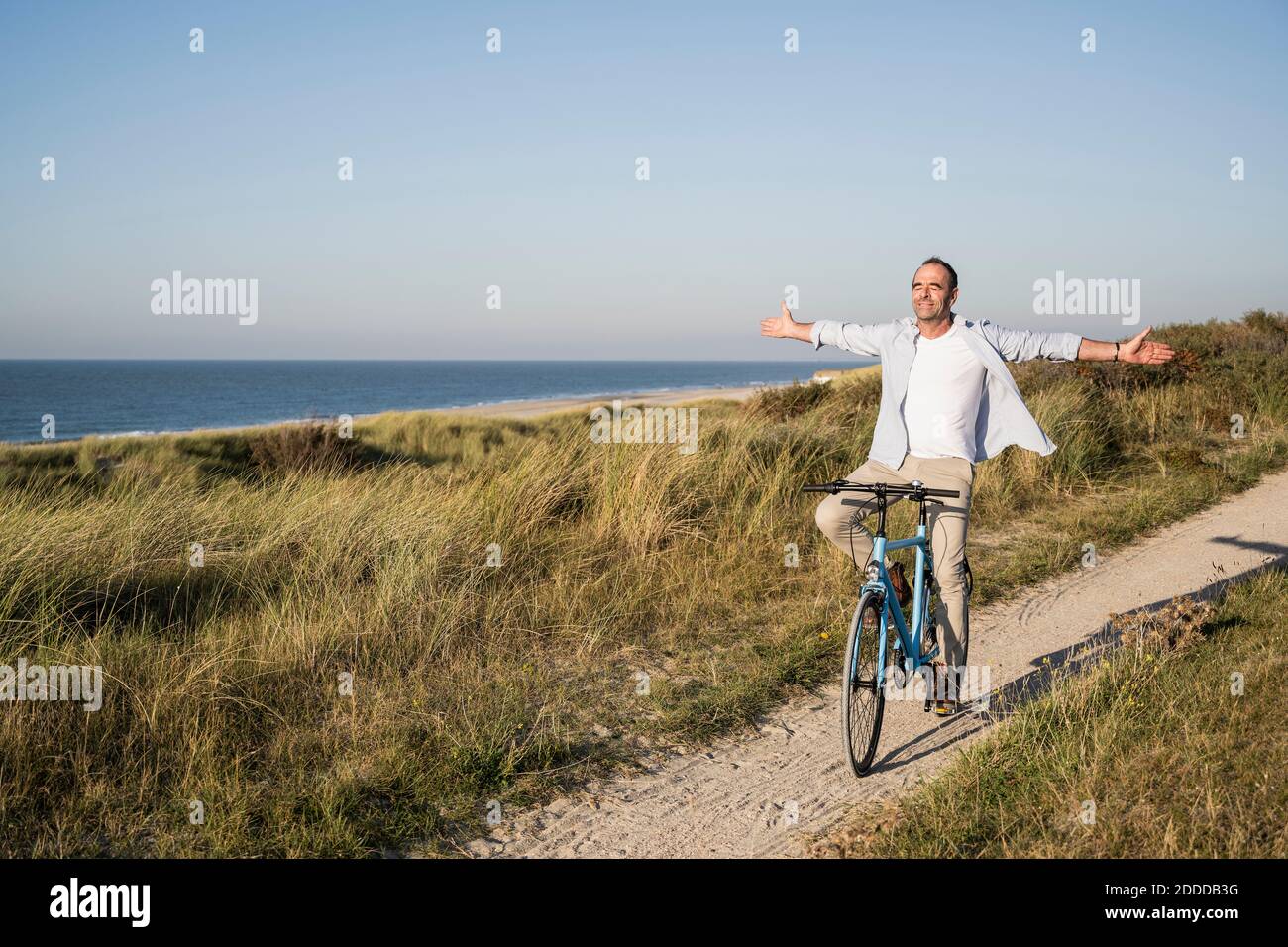 Uomo maturo spensierato con le braccia aperte che chiudono gli occhi durante la guida bicicletta in spiaggia Foto Stock