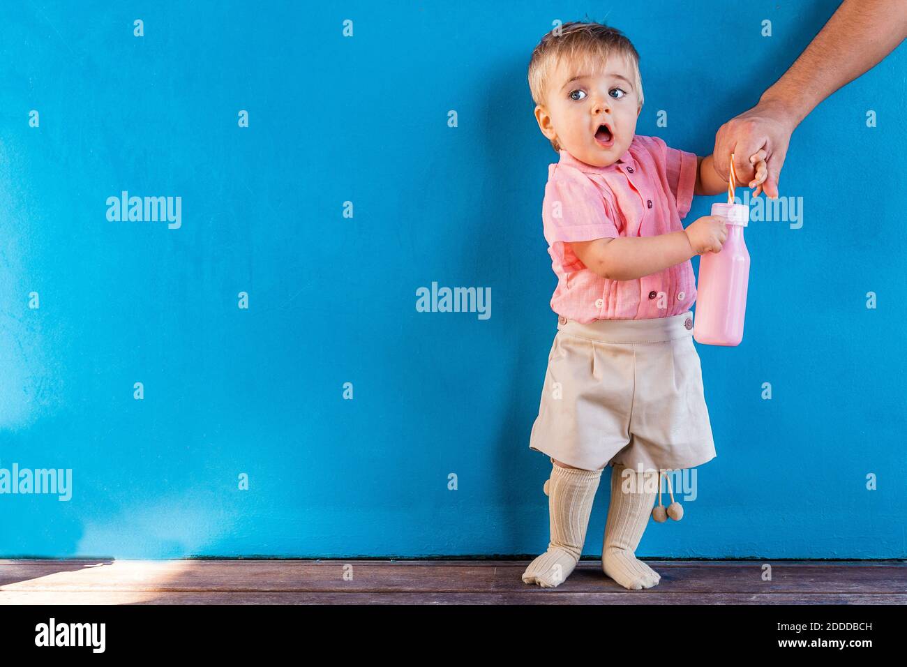 Il padre tiene la mano del bambino che fa l'espressione facciale mentre in piedi contro la parete blu Foto Stock