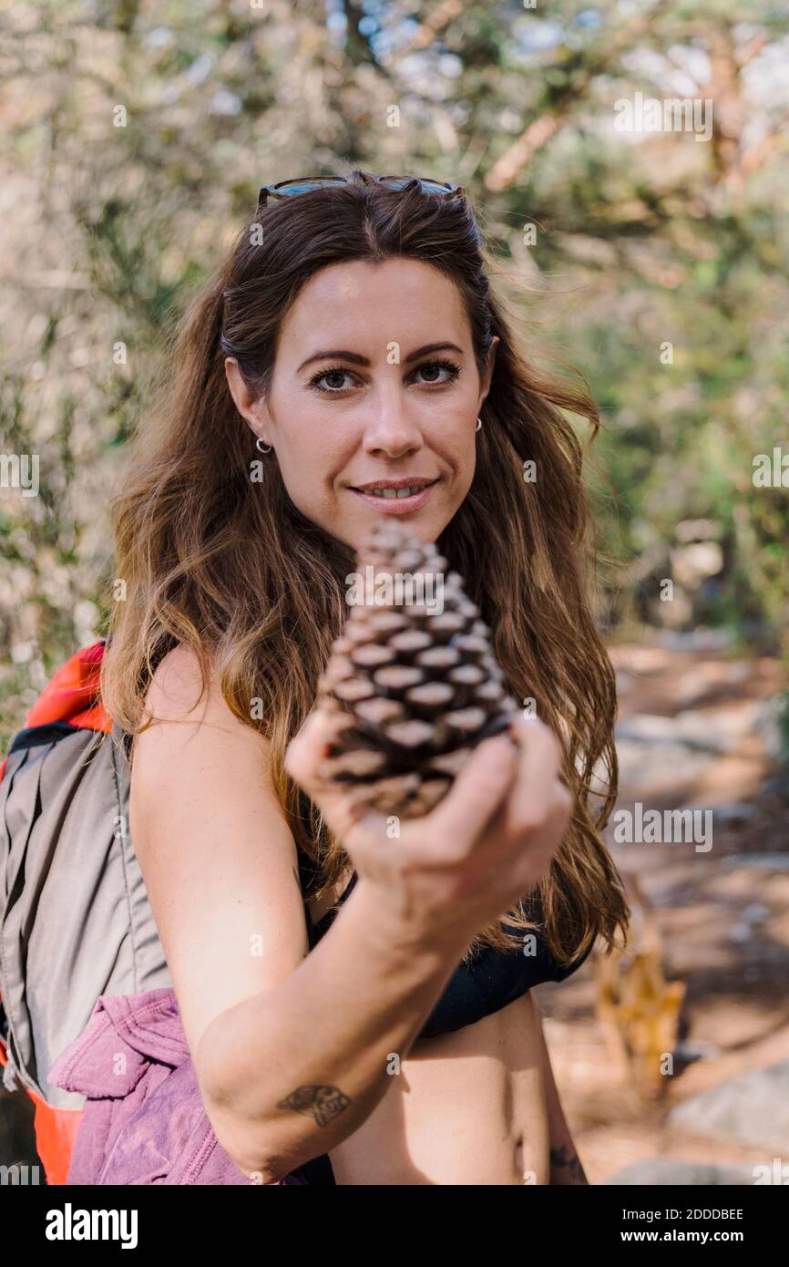Donna sorridente che tiene il cono di pino mentre si sta in piedi alla foresta Foto Stock