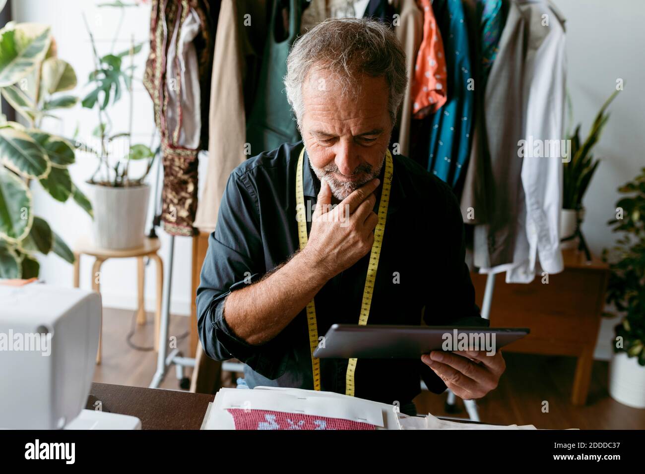 Un uomo maturo che pensa su misura mentre guarda il tablet digitale studio di lavoro Foto Stock