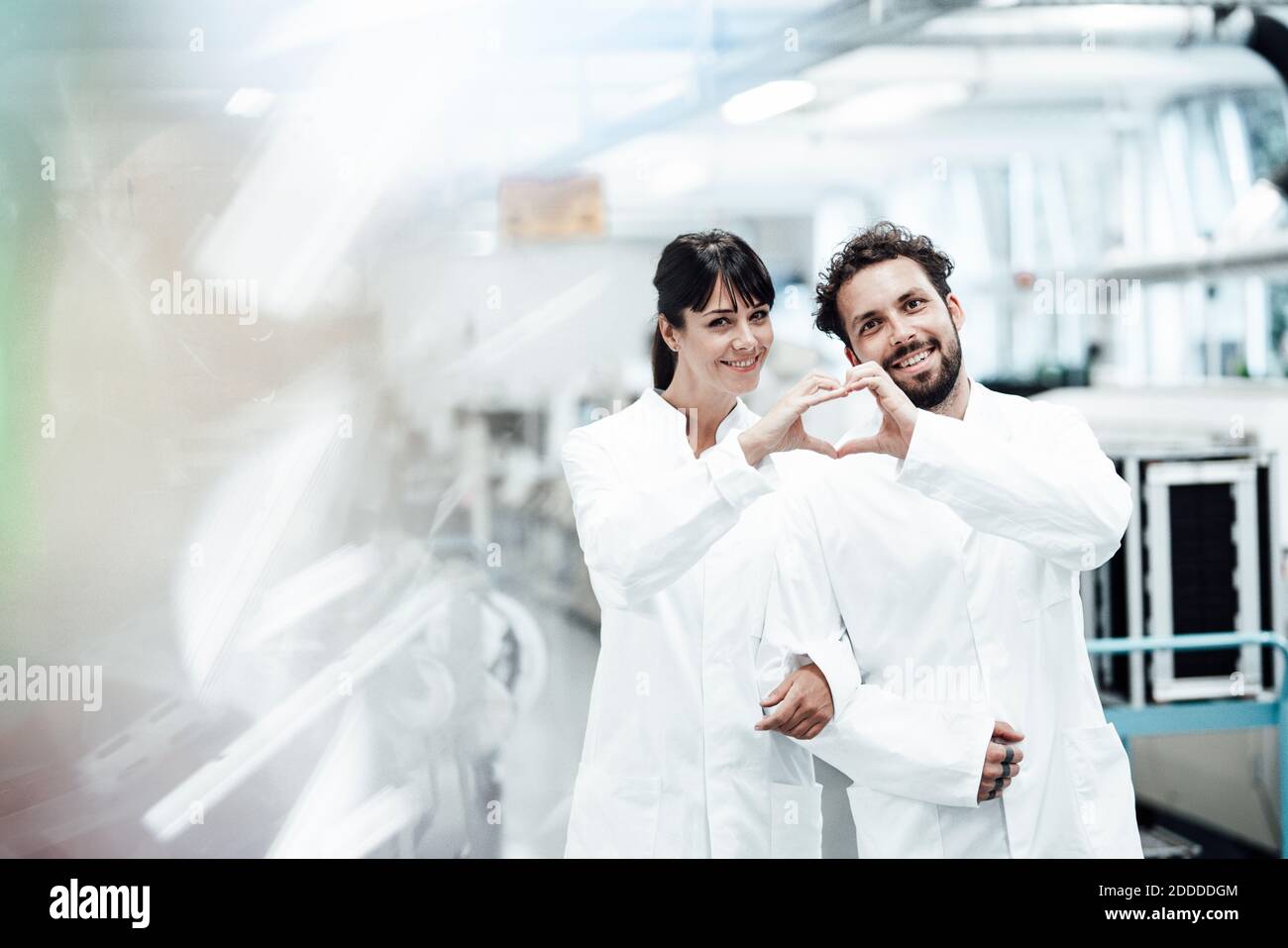 Sorridendo scienziati maschili e femminili che fanno forma del cuore con le mani mentre il braccio è in piedi nel braccio in laboratorio Foto Stock