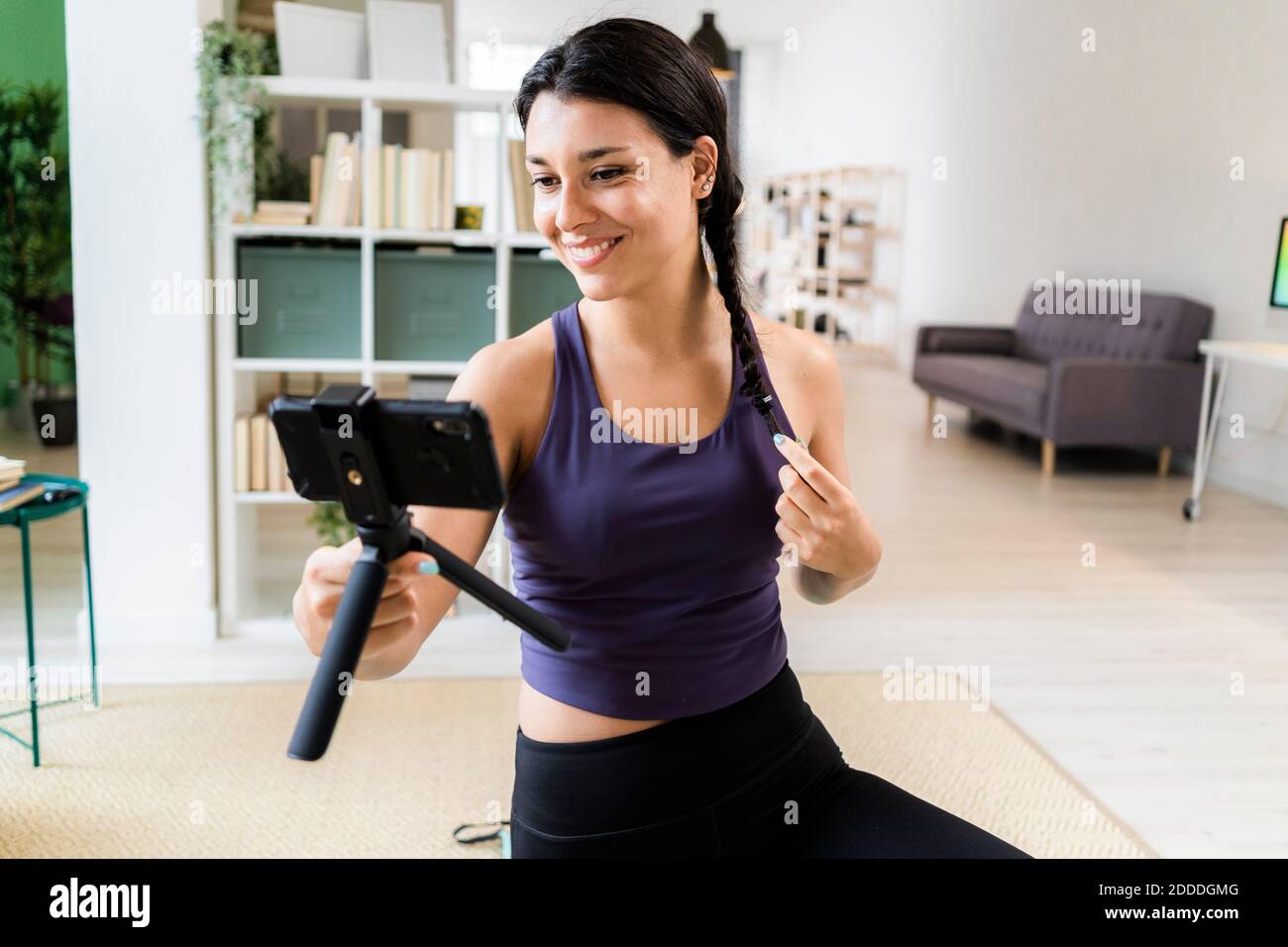Giovane donna con mani in capelli registrazione video su Smart mentre si siede a casa Foto Stock
