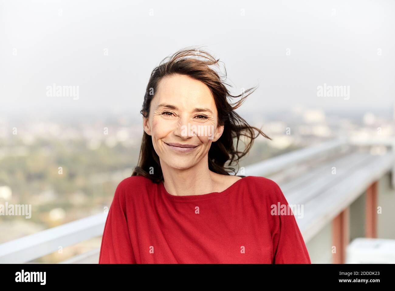 Donna sorridente con capelli che soffiano in piedi sulla terrazza dell'edificio Foto Stock
