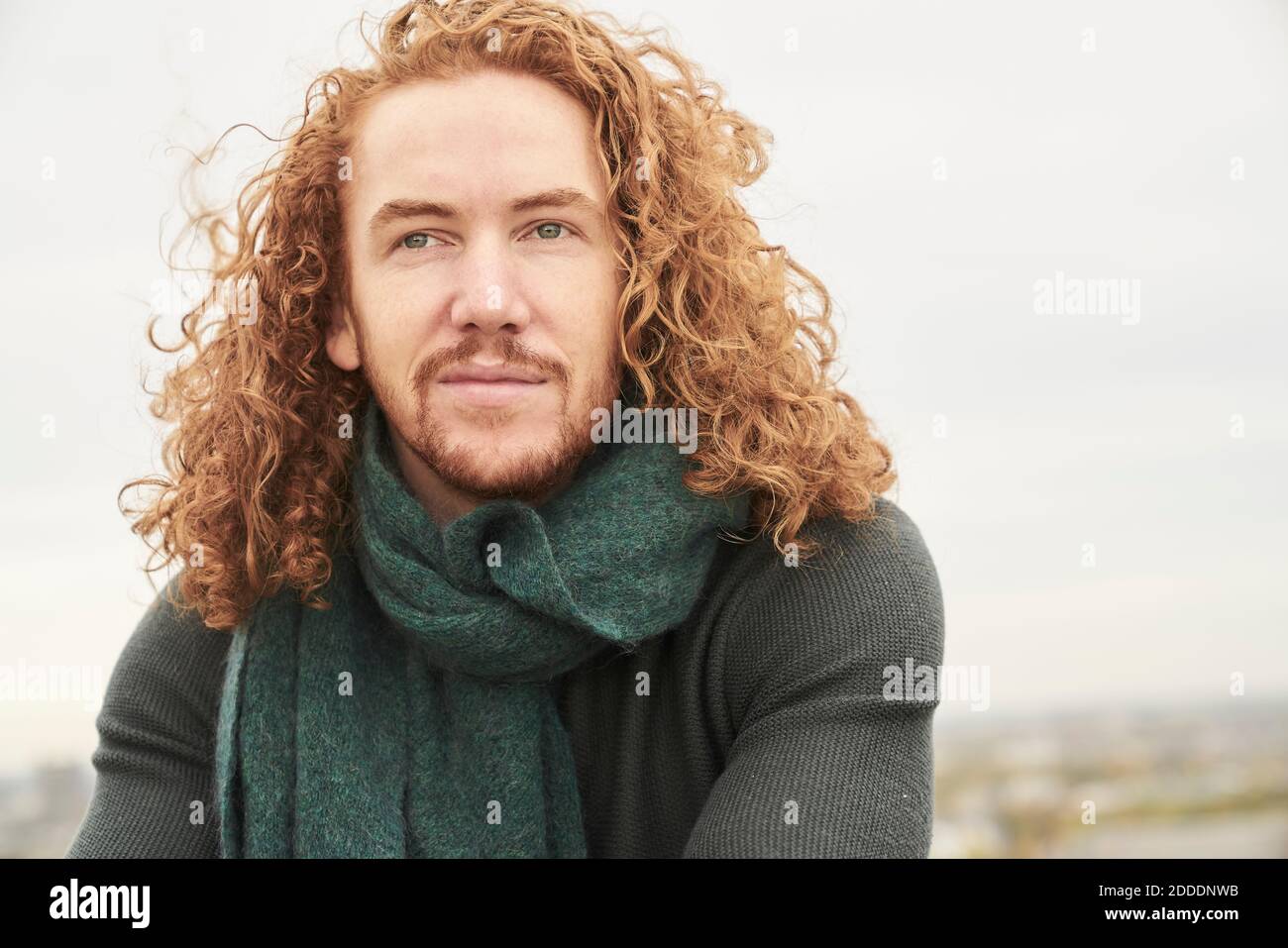 Contemplando l'uomo lungo dei capelli che guarda via contro il cielo Foto Stock