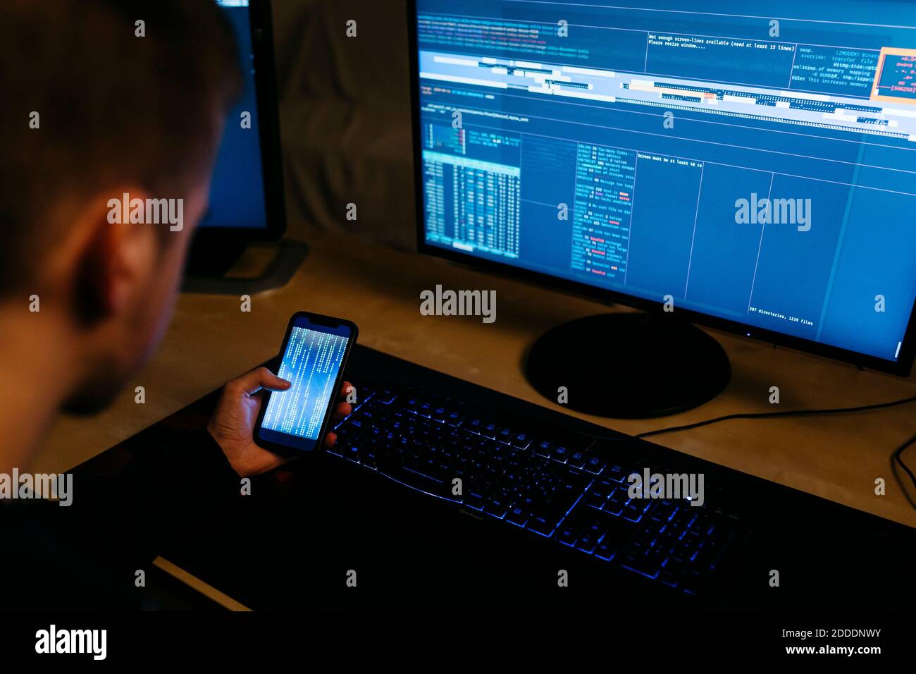 Hacker di computer maschile che utilizza il telefono cellulare mentre lavora in ufficio Foto Stock