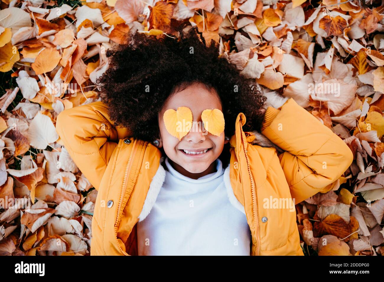 Sorridente ragazza con cuore forma foglia su occhi sdraiati foglie caduto al parco Foto Stock