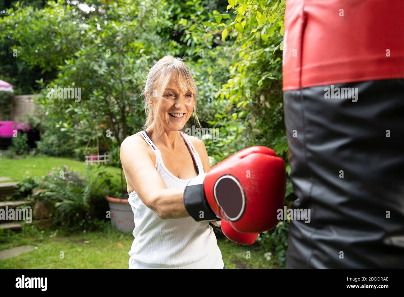 Donna anziana attiva pugno sacchetto mentre in piedi nella parte posteriore iarda in giornata di sole Foto Stock