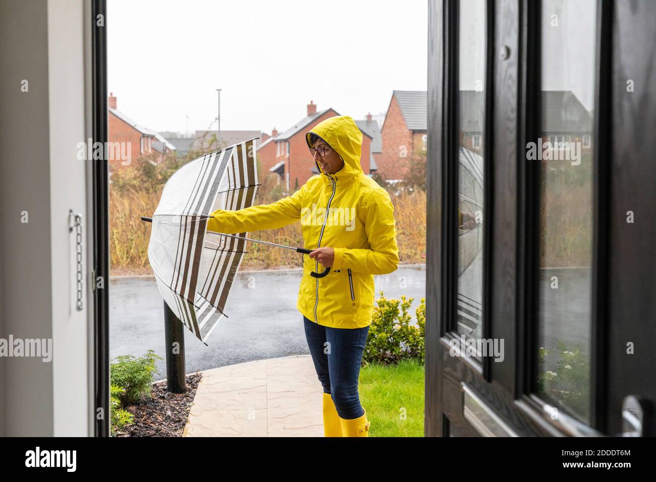 Donna mid adulta che chiude l'ombrello prima di andare a casa Foto Stock