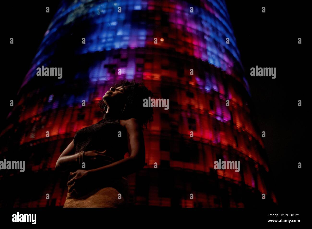 Donna premurosa in piedi contro un edificio illuminato di rosso in città Foto Stock