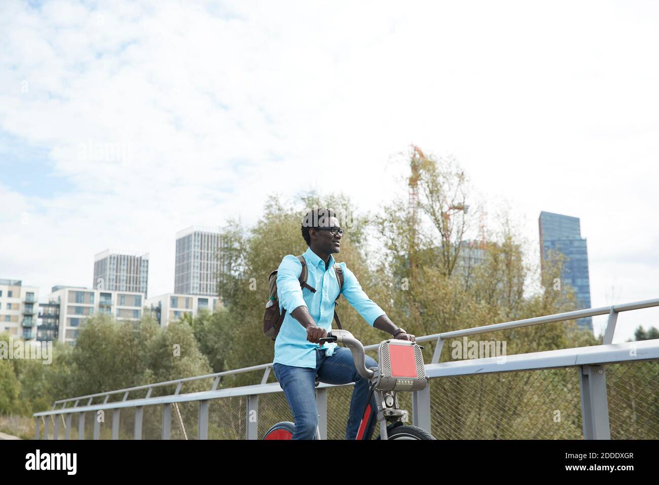 Uomo maturo che guarda via mentre si è in bicicletta contro il cielo in città Foto Stock