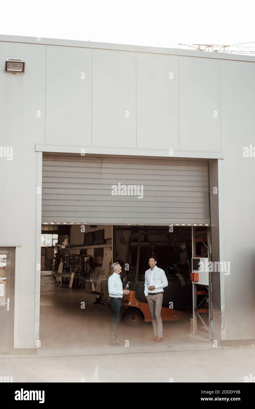 Uomini d'affari maturi che discutono mentre si levano in piedi all'entrata della fabbrica Foto Stock