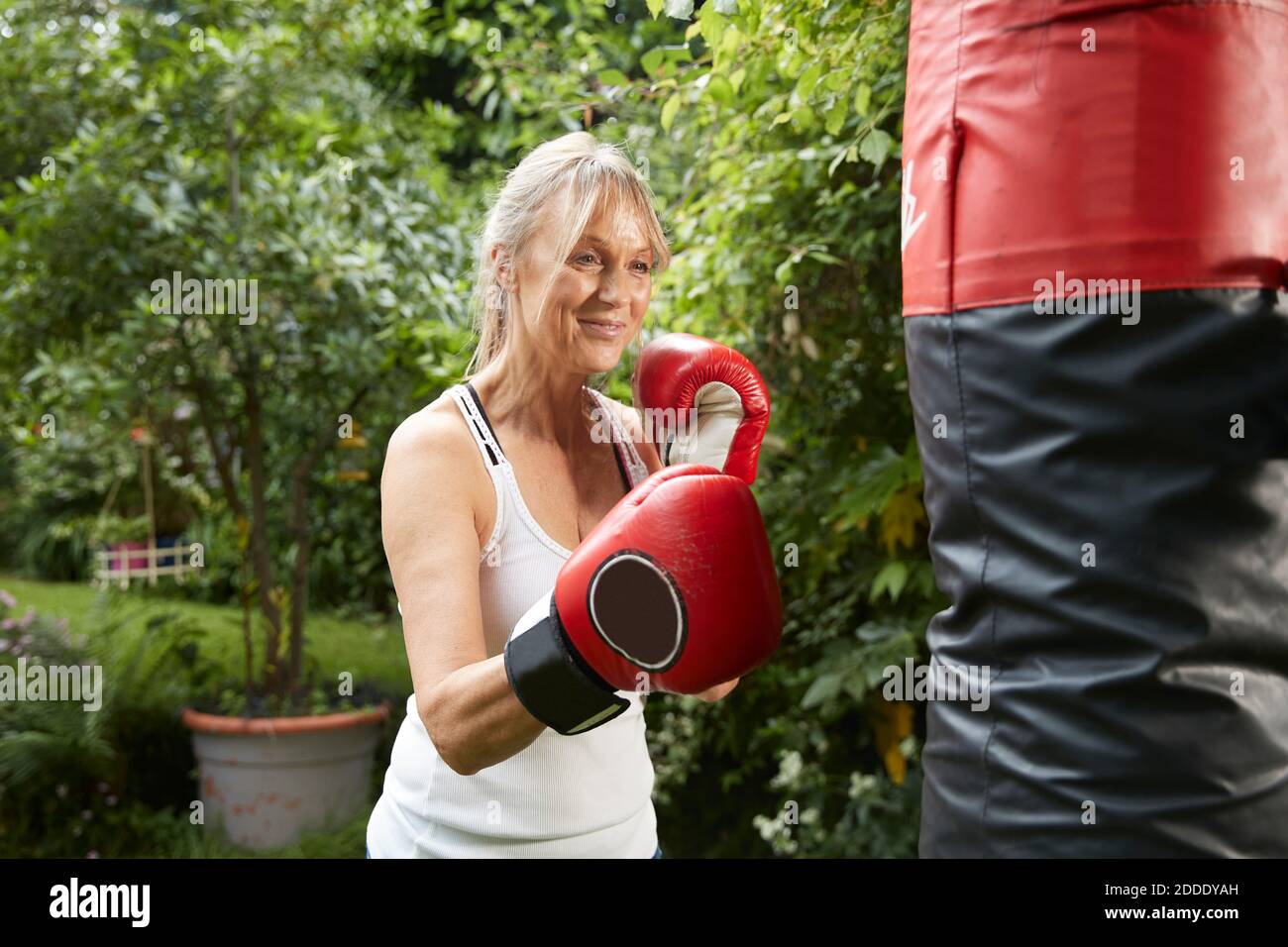 Sorridente donna anziana pugno sacchetto mentre in piedi nella parte posteriore iarda Foto Stock