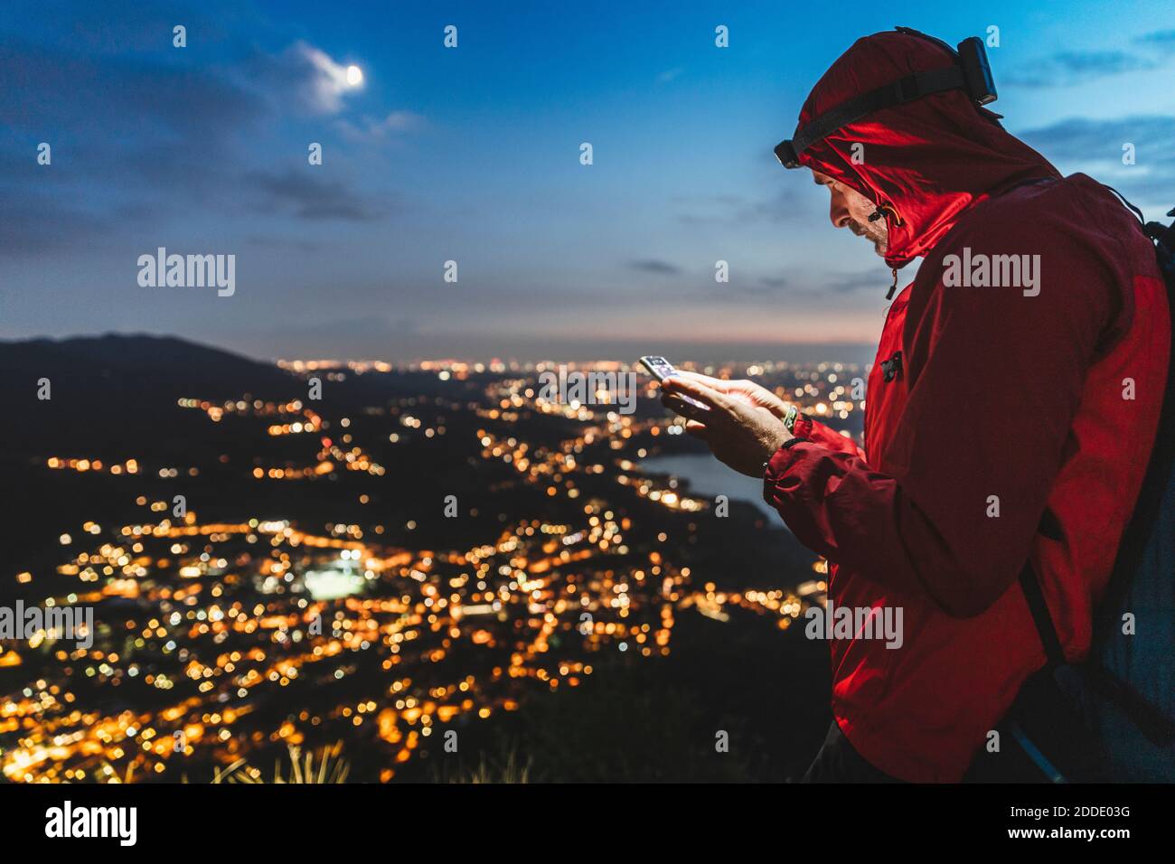 Escursionista maschile con smartphone con città illuminata contro il cielo di notte Foto Stock