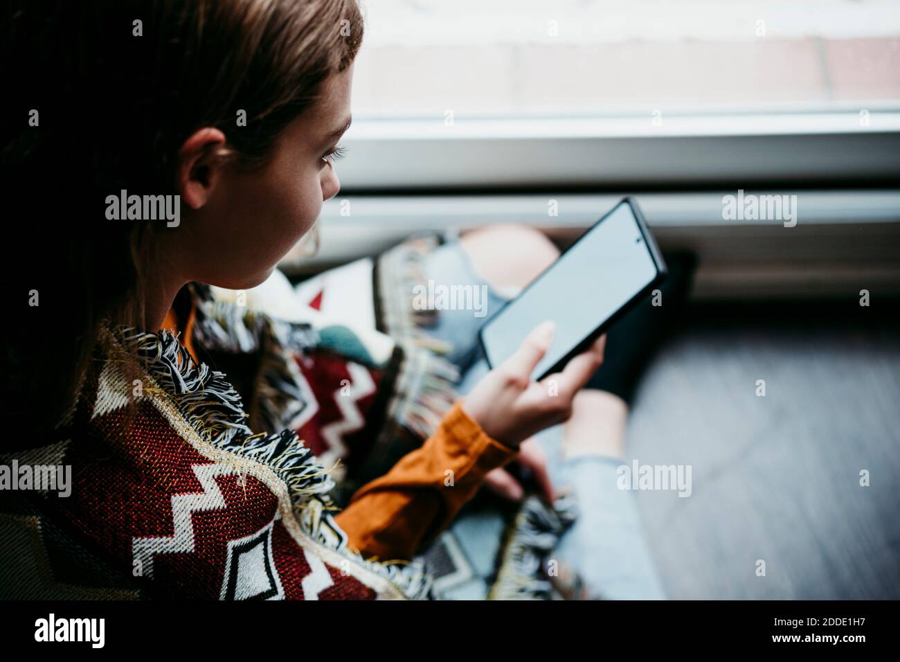 Ragazza pre-adolescente che usa il telefono cellulare mentre si siede a casa Foto Stock