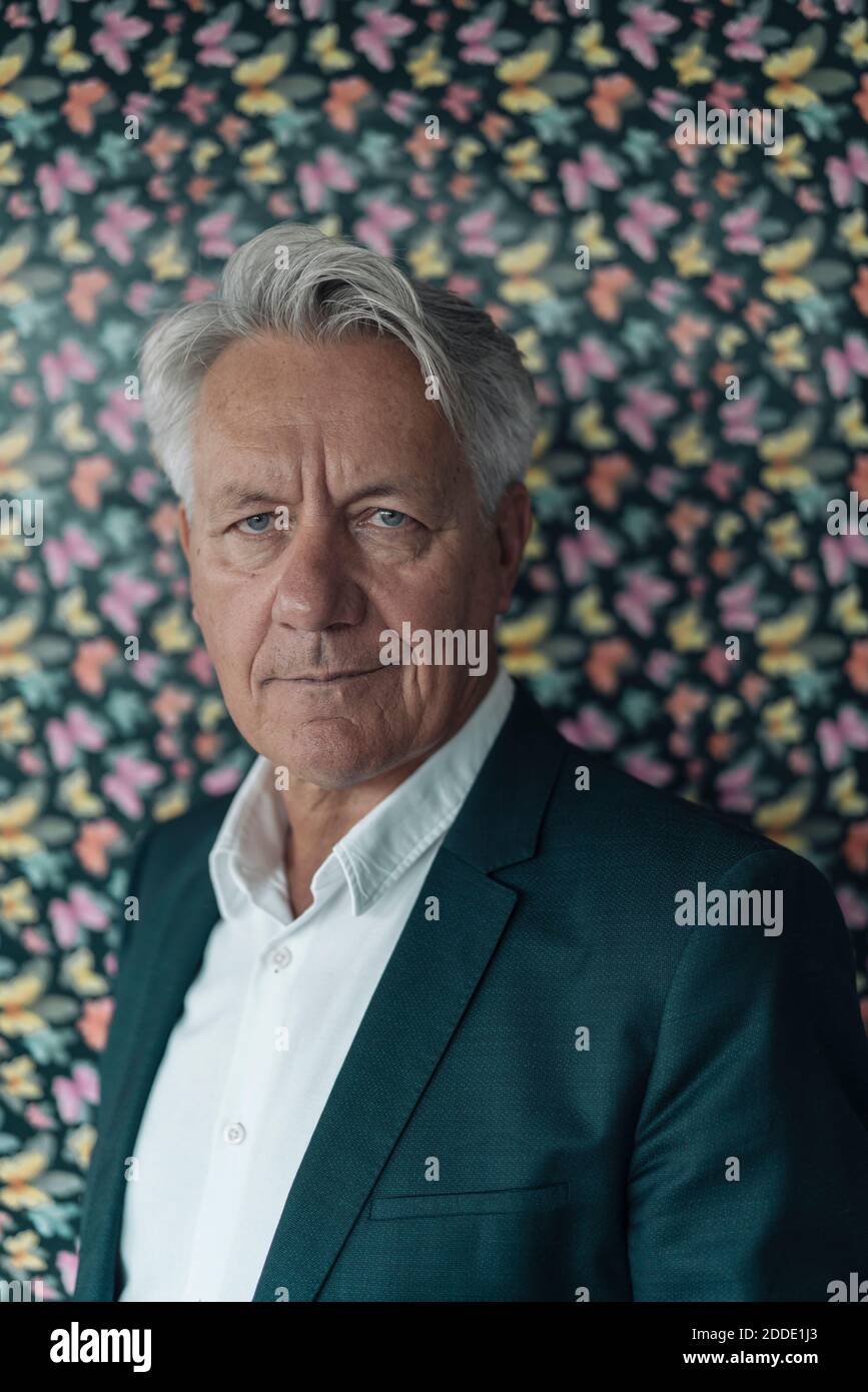 Uomo d'affari sicuro in piedi contro la parete multi colorata del modello di farfalla a. ufficio Foto Stock